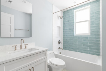 A bathroom with a white vanity cabinet, white marble countertop, and a shower with white and light...