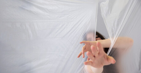 A woman reaches out from behind a translucent plastic sheet, creating a sense of mystery and...