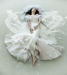 A bride in a white wedding dress lies on a painted floor, surrounded by splashes of white paint,...