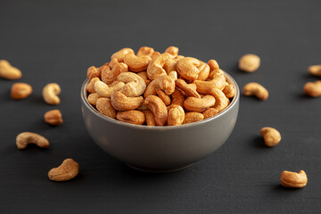 Roasted Organic Cashews in a Bowl on a black background, side view.