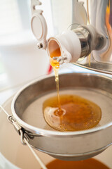 Pure Honey Flowing out of the Honey Extractor to be Filtrated with a Sieve