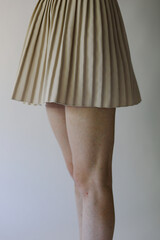 Beautiful female slender and thin legs in a yellow classic skirt on a white background. Tender fashion photography of a girl in a skirt