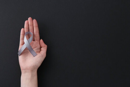 Woman with grey awareness ribbon on black background, top view. Space for text