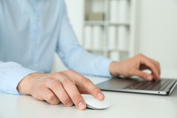 Man working with wireless mouse and laptop at white table indoors, closeup