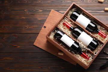Box with wine bottles, corkscrew and corks on wooden table, flat lay. Space for text