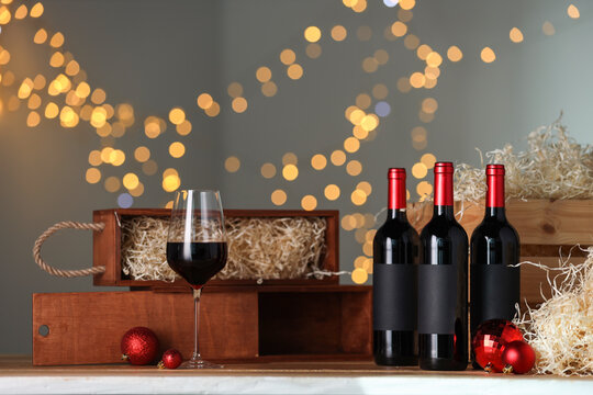 Bottles of wine, glass, wooden gift boxes and red Christmas balls on table