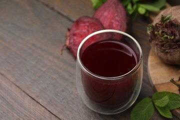 Fresh beet juice in glass, ripe vegetables and mint on wooden table, closeup. Space for text