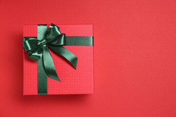 Gift box with green bow on red background, top view. Space for text