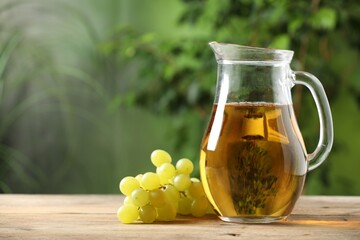 Tasty juice in glass jug and grapes on wooden table outdoors, space for text