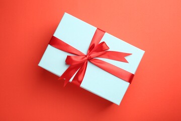 Gift box with red bow on coral background, top view