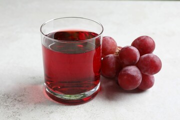 Tasty grape juice in glass and berries on light textured table, closeup