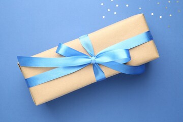 Gift box with bow and confetti on blue background, top view