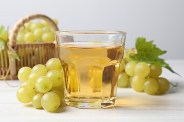 Ripe grapes and glass of tasty juice on white wooden table