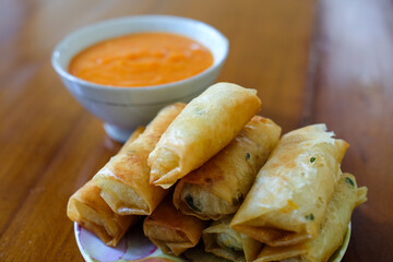 Fried spring rolls on white plate, served with chili sauce sambal on top the wood table, traditional snack, Traditional spring rolls, copy space .