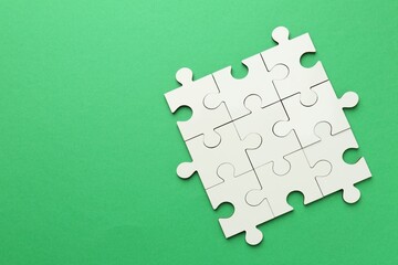 White puzzle pieces on green background, top view. Space for text