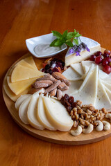 Table of different cheeses presented with grapes, nuts, some mint leaves and lavender flowers