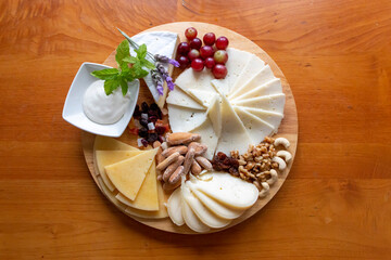Table of different cheeses presented with grapes, nuts, some mint leaves and lavender flowers