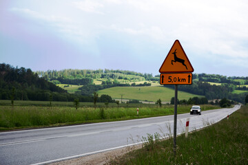 Znak drogowy, samochód osobowy na drodze ekspresowej wśród zielonych pól i gór zarośniętych lasem. © Stanisław Błachowicz