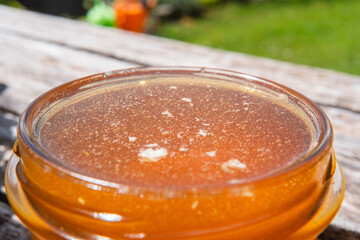 Open Honey Jar Filled with Bee Honey Standing Outside on a Wooden Table in the Garden on a Hot Sunny Summer Day Extreme Close Up