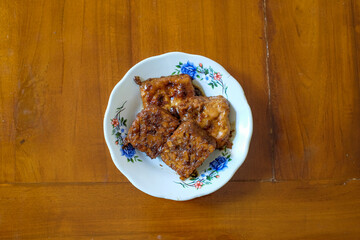 Tempeh and Tahu Bacem in white plate on the wood table, traditional Indonesian dishes with a sweet taste.