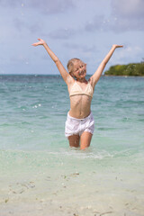 Girl having fun splashing in the ocean, water splashes, white sand, blue water, exotic summer vacation