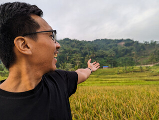 Close up A Southeast Asian man traveler face and hand pointing on yellow rice fields in Bandung, happy holidays.