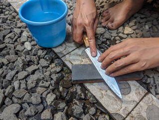 Closeup man hands sharpen knife on whetstone sharpener or grindstone in outdoors. Concept,...