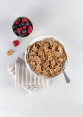 Whole grain corn flakes in a white bowl and fresh berries on a white background. Fitness breakfast.