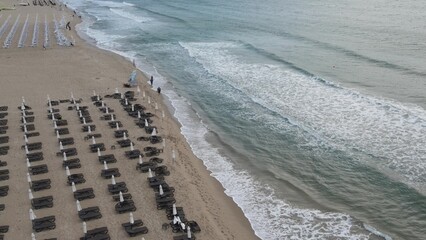Beautiful beach on seashore, sun loungers stand on shore for sunbathing, people walk, play sports