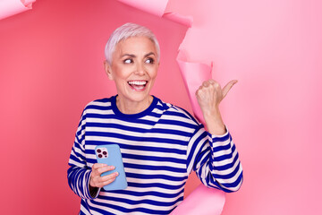 Photo of charming adorable woman wear striped clothes breaking paper wall presenting empty space...