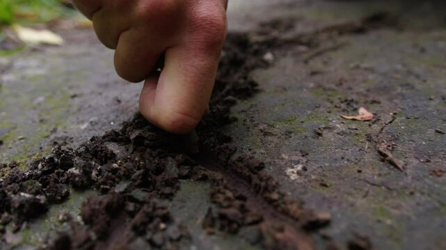 A man's hand writes on the ground with a stick. Close-up. Ancient drawings and symbols.