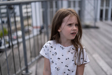 A small beautiful schoolgirl without one front tooth stands with concentration on a wooden terrace...