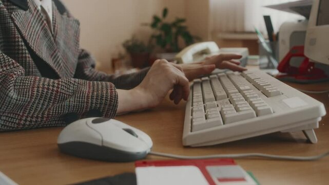 Side midsection shot of faceless clerical worker working on retro computer, using keyboard and old wired mouse, floppy discs on desk, nostalgic 90s office