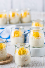 Coconut rice pudding with mango in dessert glasses on white wooden background, vertical