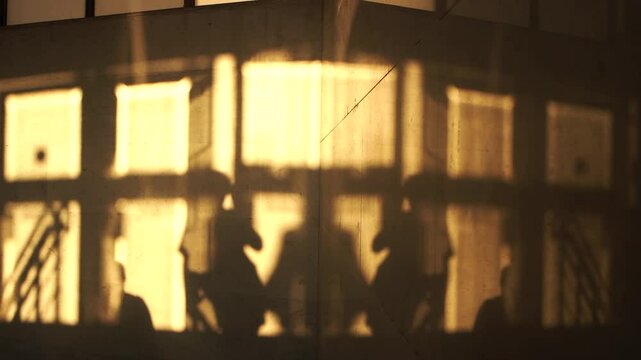 Shadows of people on a marble wall walking into an underpass during sunset in the city 4K