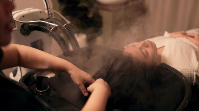 A woman customer get service hair care in procedure of steaming water steam and feeling relax while hairdresser massaging head at beauty salon.
