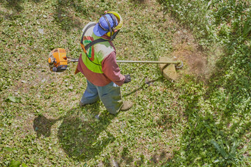 A gardener in a safety helmet and work overalls with a lawnmower brings the lawn to order.