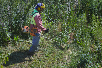 The lawnmower operator in overalls and a helmet works on the lawn.