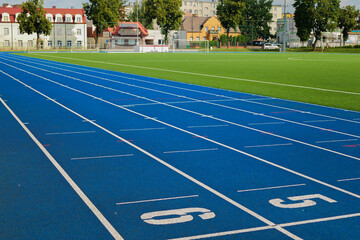 Soccer field with artificial green grass, with white goals. There are running tracks with a blue surface around it. Surrounding the stadium is a residential area with white brick houses 