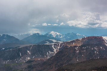 Scenic landscape with beautiful large snow-capped peaked top in rainy low clouds. Dramatic alpine view to high mountains under cloudy sky. Big snowy mountain range in rain. Colorful sharp sheer crags.