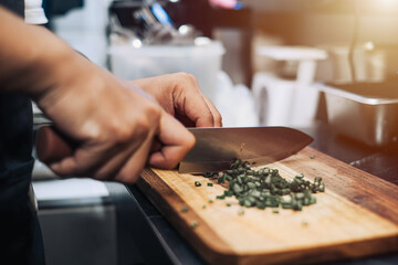 Close-up shot of a hand cutting out leeks using a knife on the wooden cutting board with bokeh background