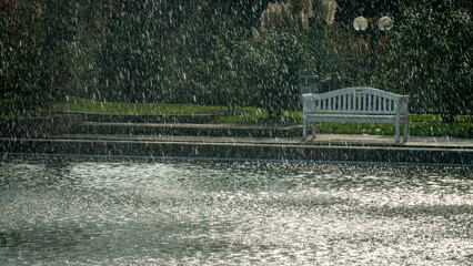 Fountain in a public park with a white bench in the background