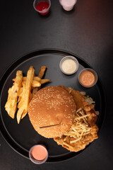 Crispy chicken burger on black background. Tomato, lettuce, chicken burger, sauces and fries.