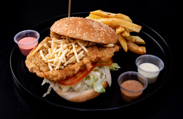 Crispy chicken burger on black background. Tomato, lettuce, chicken burger, sauces and fries.