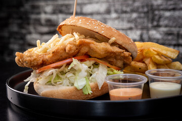 Crispy chicken burger on black background. Tomato, lettuce, chicken burger, sauces and fries.
