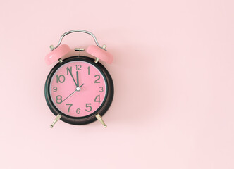 Pastel pink and black alarm clock on light pastel pink background with copy space. Minimal time concept. Flat lay.