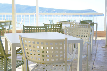 Empty tables and chairs of a street cafe located on the sea coast. Free seats on the cafe terrace early in the morning.