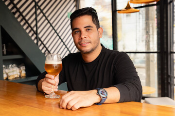 Smiling man looking at camera with a beer at the bar in a modern bar with stylish interior.