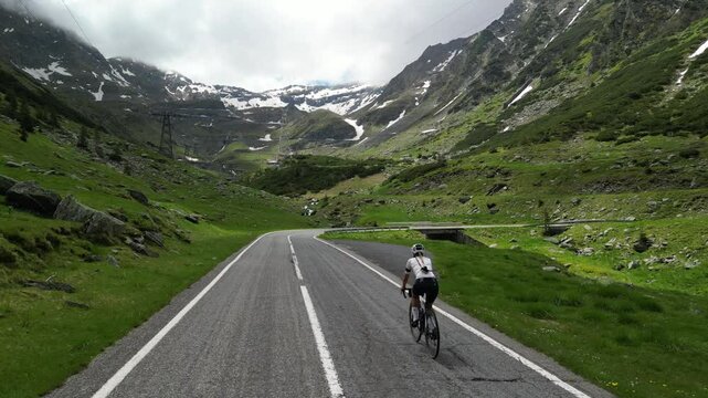 Aerial drone shot of female cyclist pushing pedals on bicycle up an asphalt road in mountains with amazing view. Cycling on a serpentine road.  Sport motivation. Active sport. Transfagarasan, Romania
