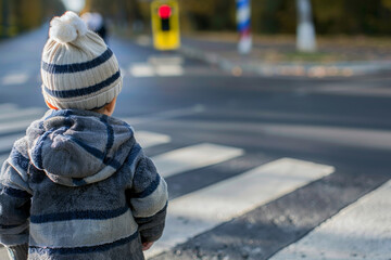 A young boy is standing at a crosswalk, looking at the traffic lights